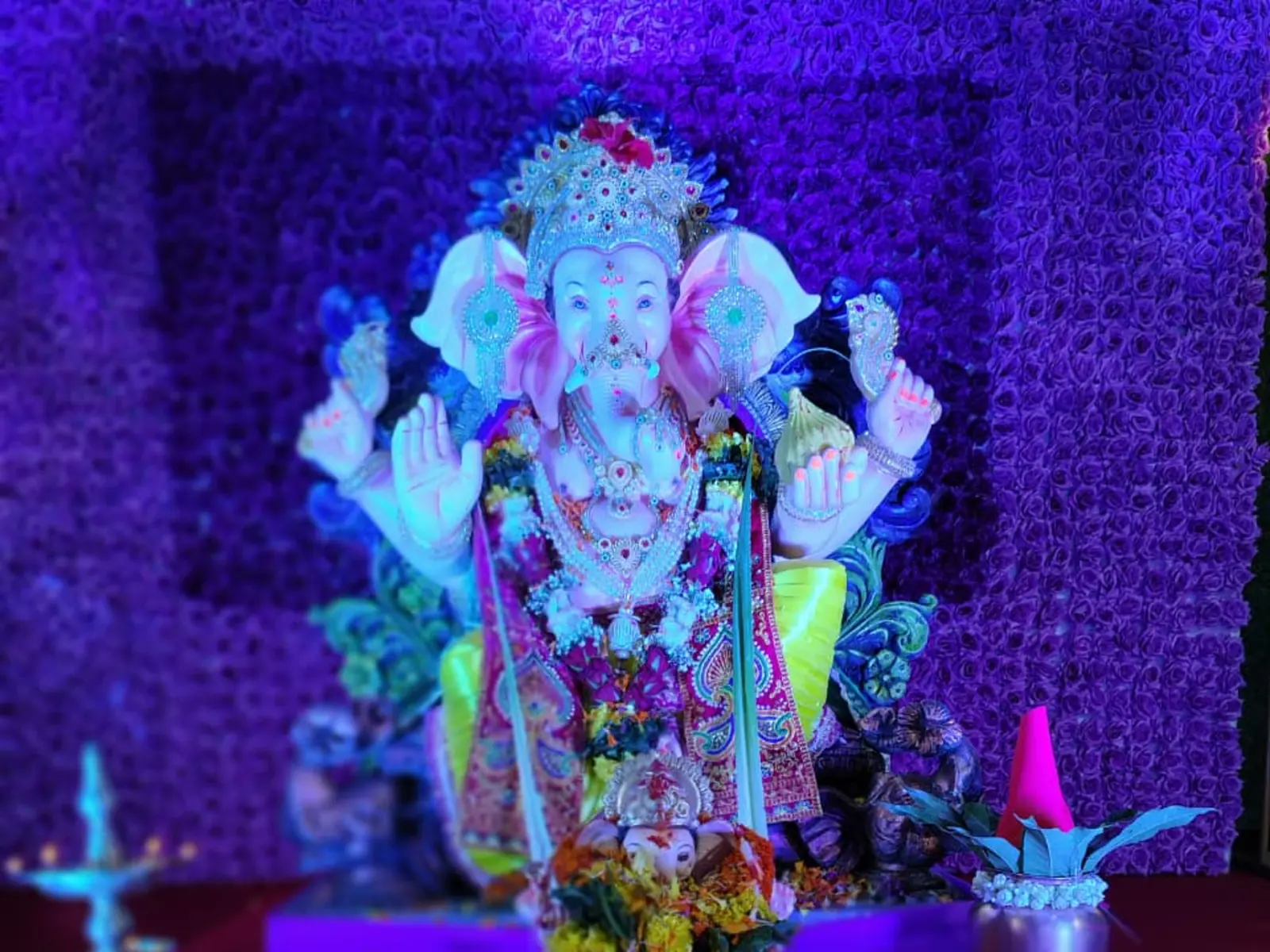 A decorated Ganesha idol surrounded by flowers, offerings and ceremonial lighting.
